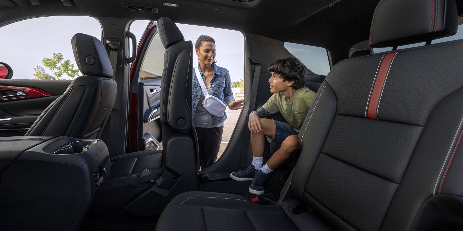 A woman and boy in a car's black leather interior, she stands at the tilted-forward second-row seat, he sits in the third.