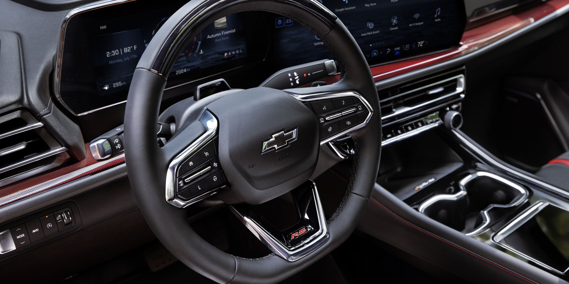View of a Chevrolet steering wheel and a portion of the dashboard and center console with red accents.