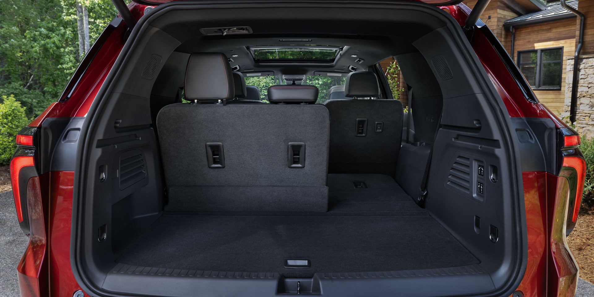 View of the back of a red SUV with the trunk open, revealing gray seats, the right one folded down.