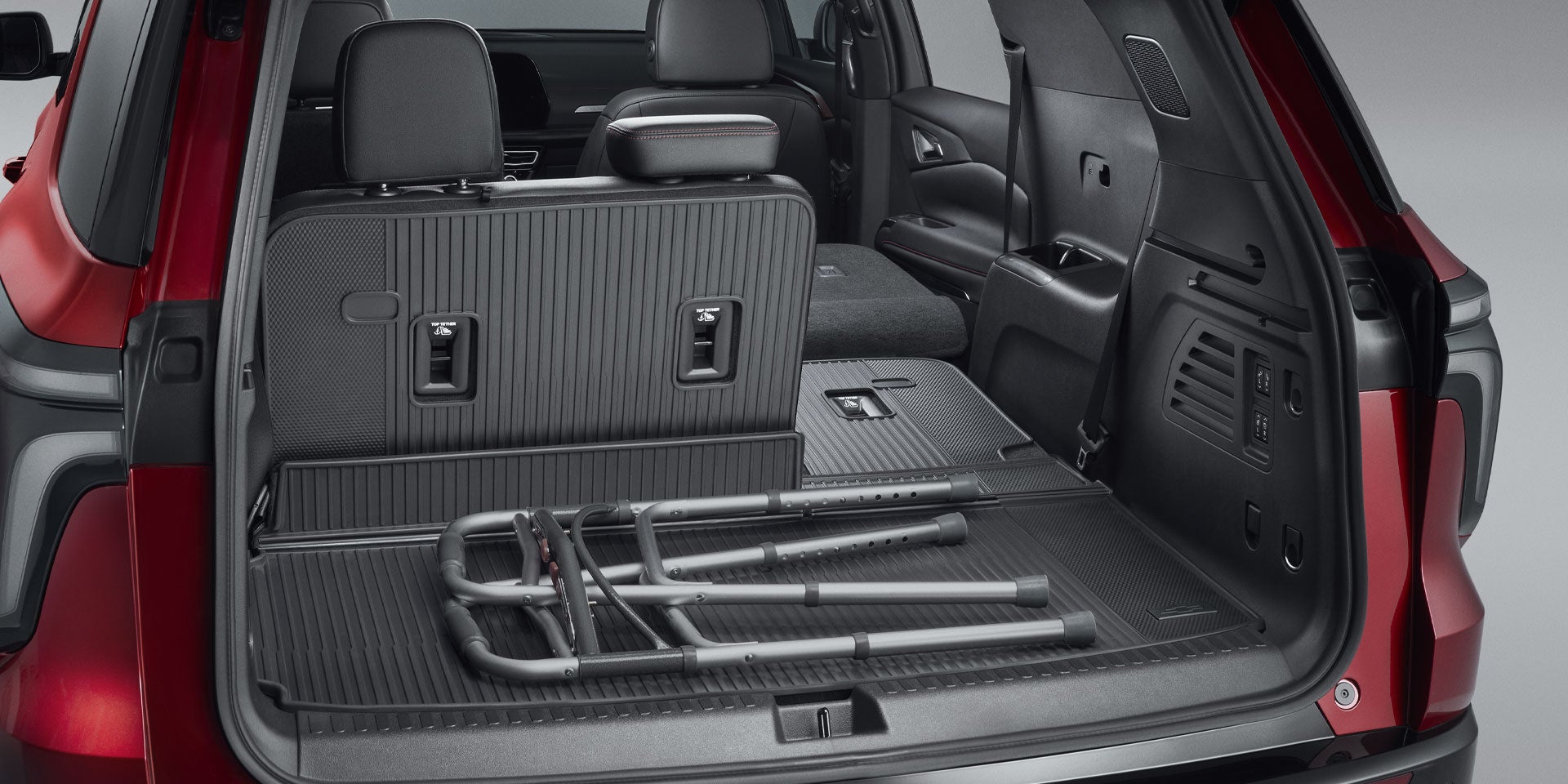 Rear cargo area of a red SUV with folded third-row seat, a folded walker, and a retractable cargo liner.